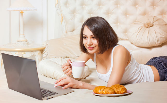 Jeune femme sédentaire consultant internet dans son lit avec des friandises